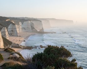 À l’aube, un rivage français calme avec des falaises de calcaire, une plage et un sentier côtier sinueux baignés de lumière douce.