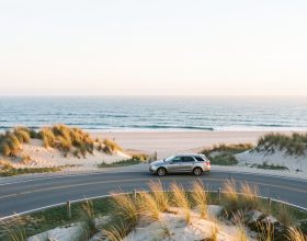 Une voiture discrète roule sur une route côtière de Cape Cod au lever du soleil, entre les dunes blondes et l’océan Atlantique.