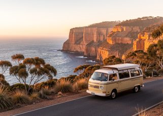 Un van de voyage stationné sur une route côtière australienne au coucher du soleil, avec des falaises, l’océan et une végétation automnale éclairés par une lumière douce.